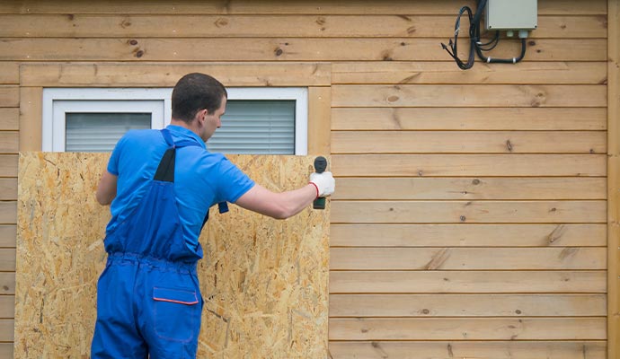 worker boarding up a window on a house