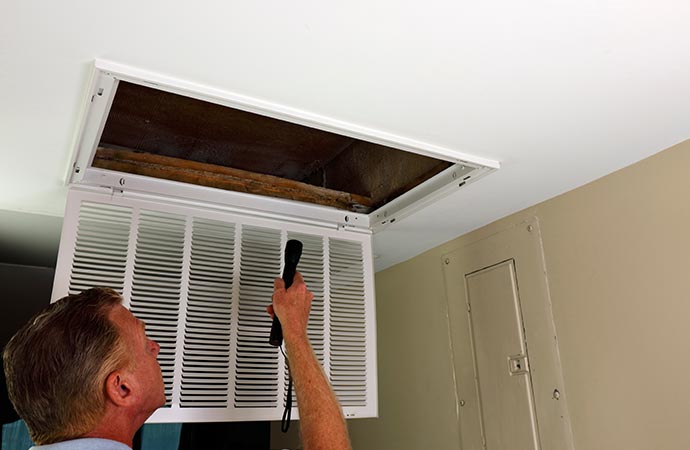 A man inspecting air duct with his torch light