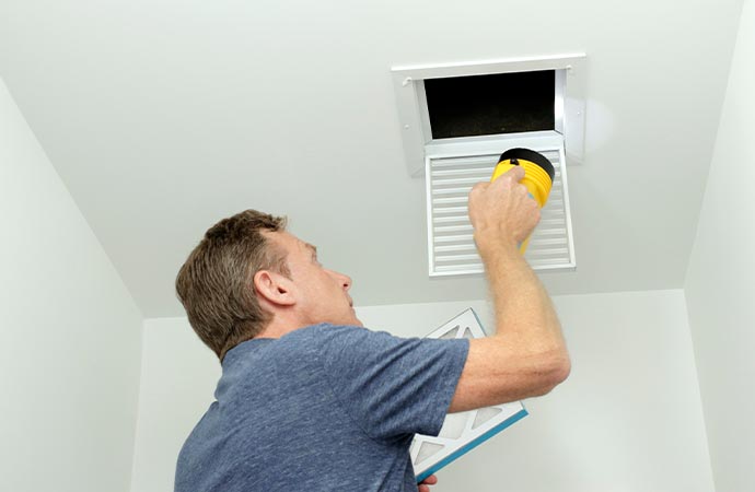 Man checking air duct in home